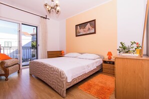 Ein Schlafzimmer mit Bett, Stuhl, Schreibtisch, Kommode, einem Gemälde und einem Balkon.
