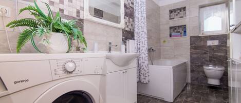 Een moderne badkamer met een wasmachine, een douche, een toilet en een wastafel.