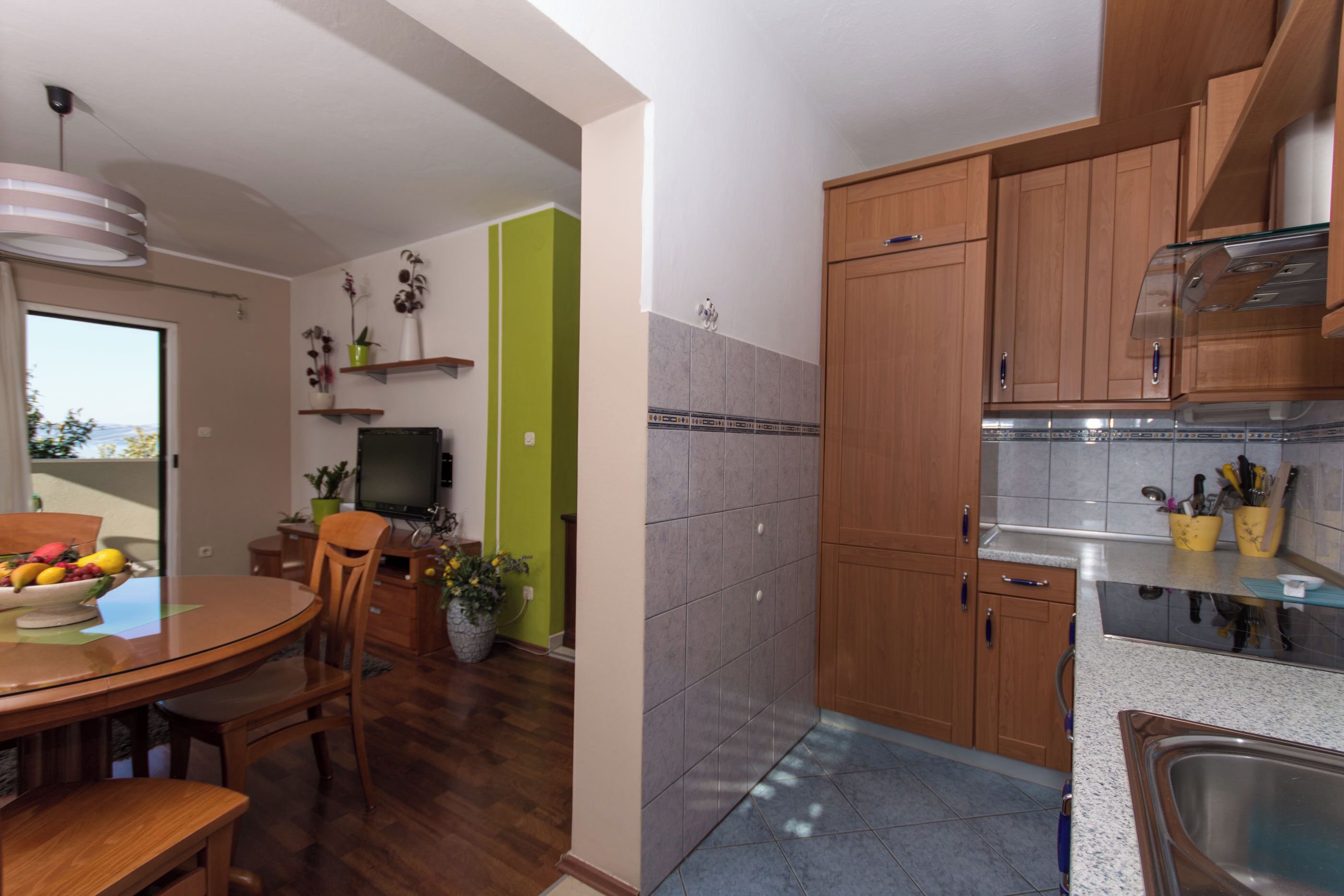 A modern kitchen with wooden cabinets, a stainless steel sink, and a dining area with a round table and chairs.