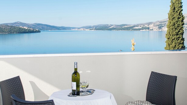 A table with a bottle of wine and glasses, overlooking a calm lake with mountains in the background. - Apartment MM (Okrug)