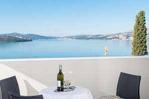 A table with a bottle of wine and glasses, overlooking a calm lake with mountains in the background. - Apartment MM (Okrug)