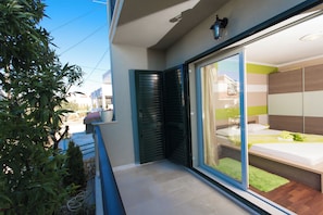 Un apartamento moderno con balcón, puerta corredera de vidrio que da a un dormitorio y una pequeña zona ajardinada.