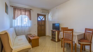 A living room with a sofa, a wooden table with chairs, a television, and a window with curtains. - Apartments Dino (Crikvenica)