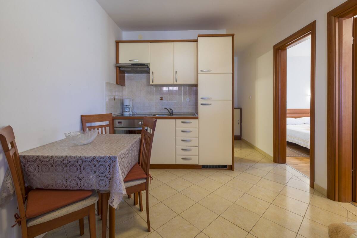 A compact kitchen with a dining table, chairs, and a refrigerator.