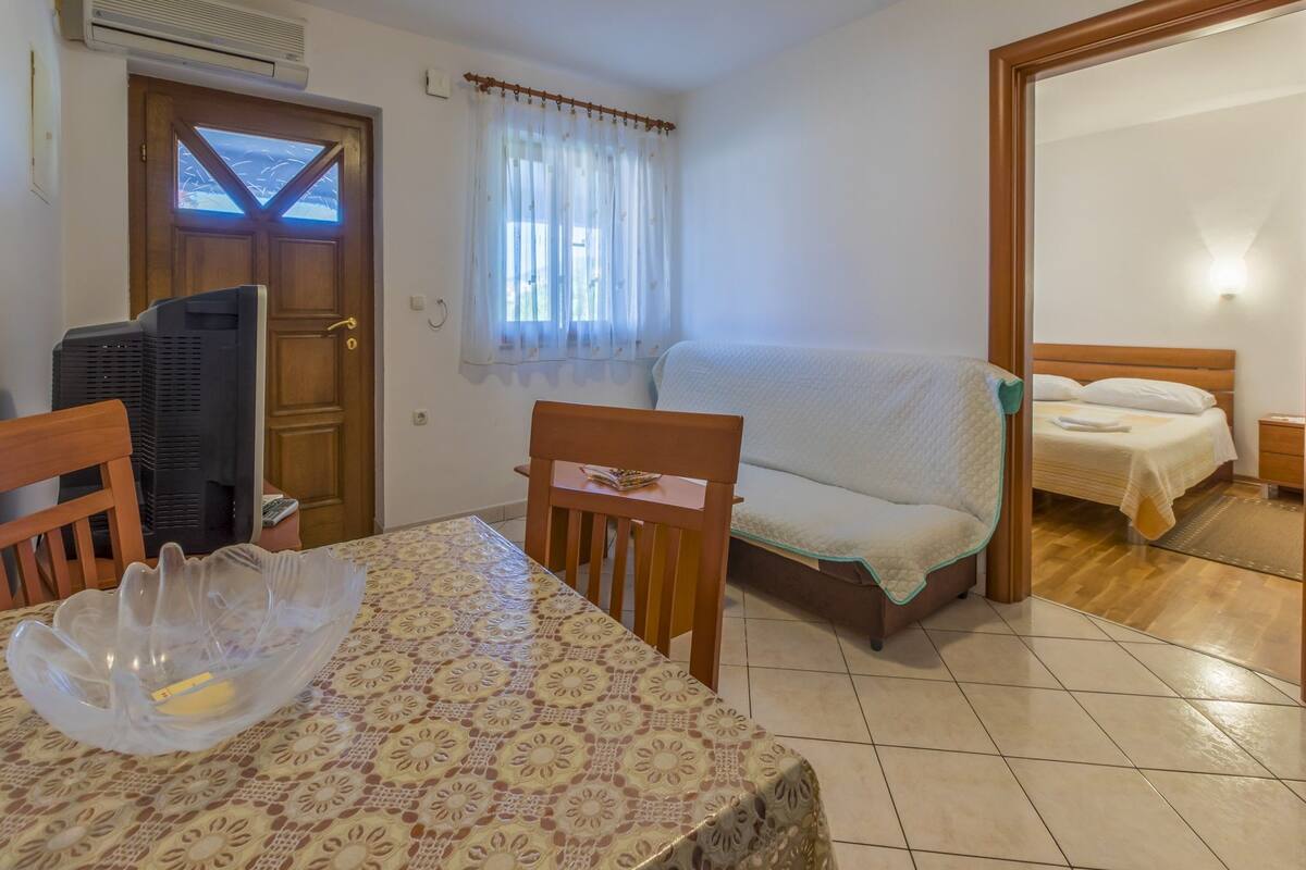 A compact room with a bed, a sofa, a dining table, and a TV.