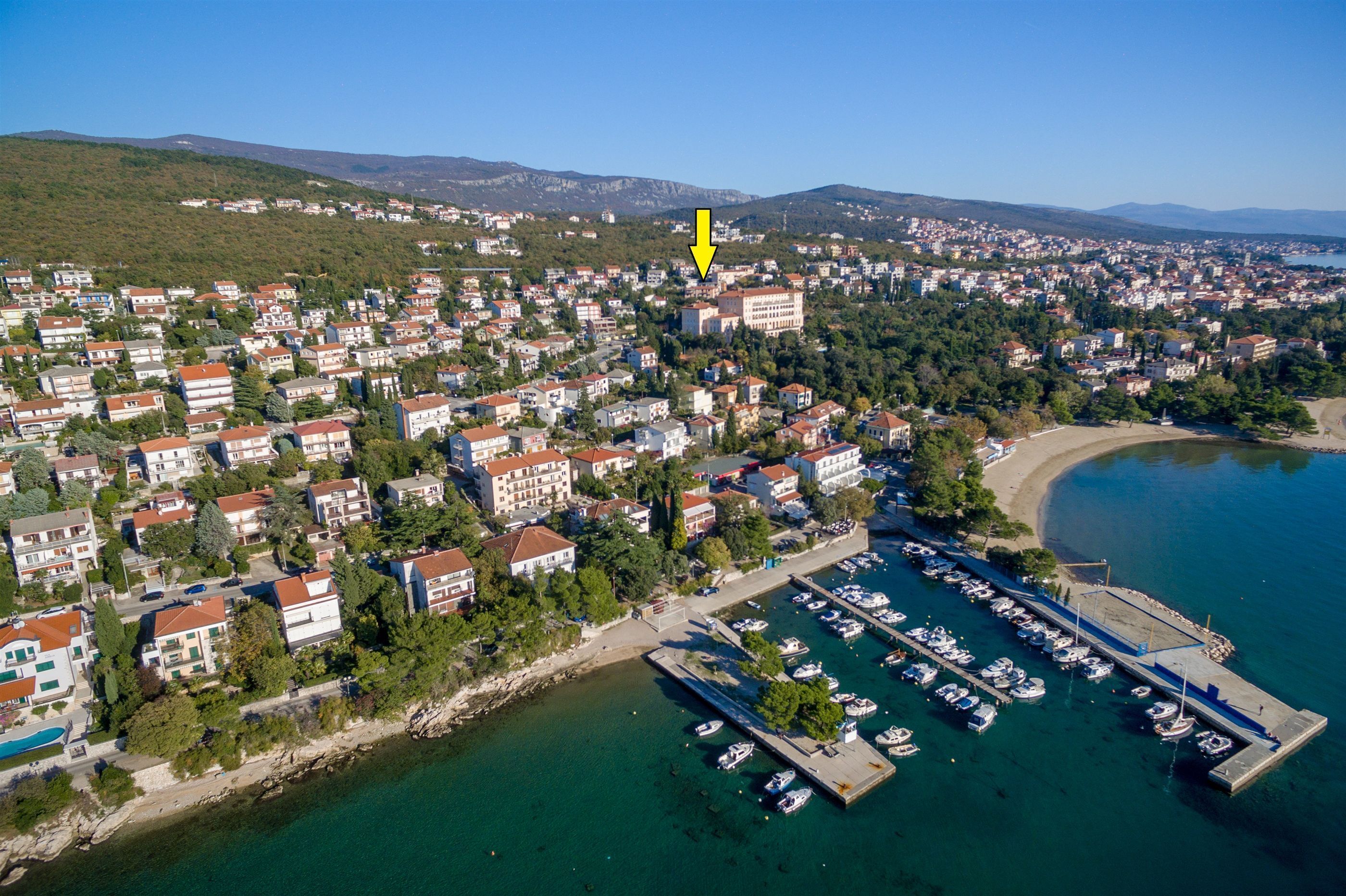 An aerial view of a coastal town with residential buildings, a marina with boats, and a beach.
