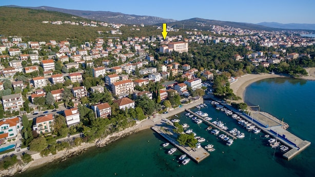 An aerial view of a coastal town with residential buildings, a marina with boats, and a beach. - Apartments Dino (Crikvenica)