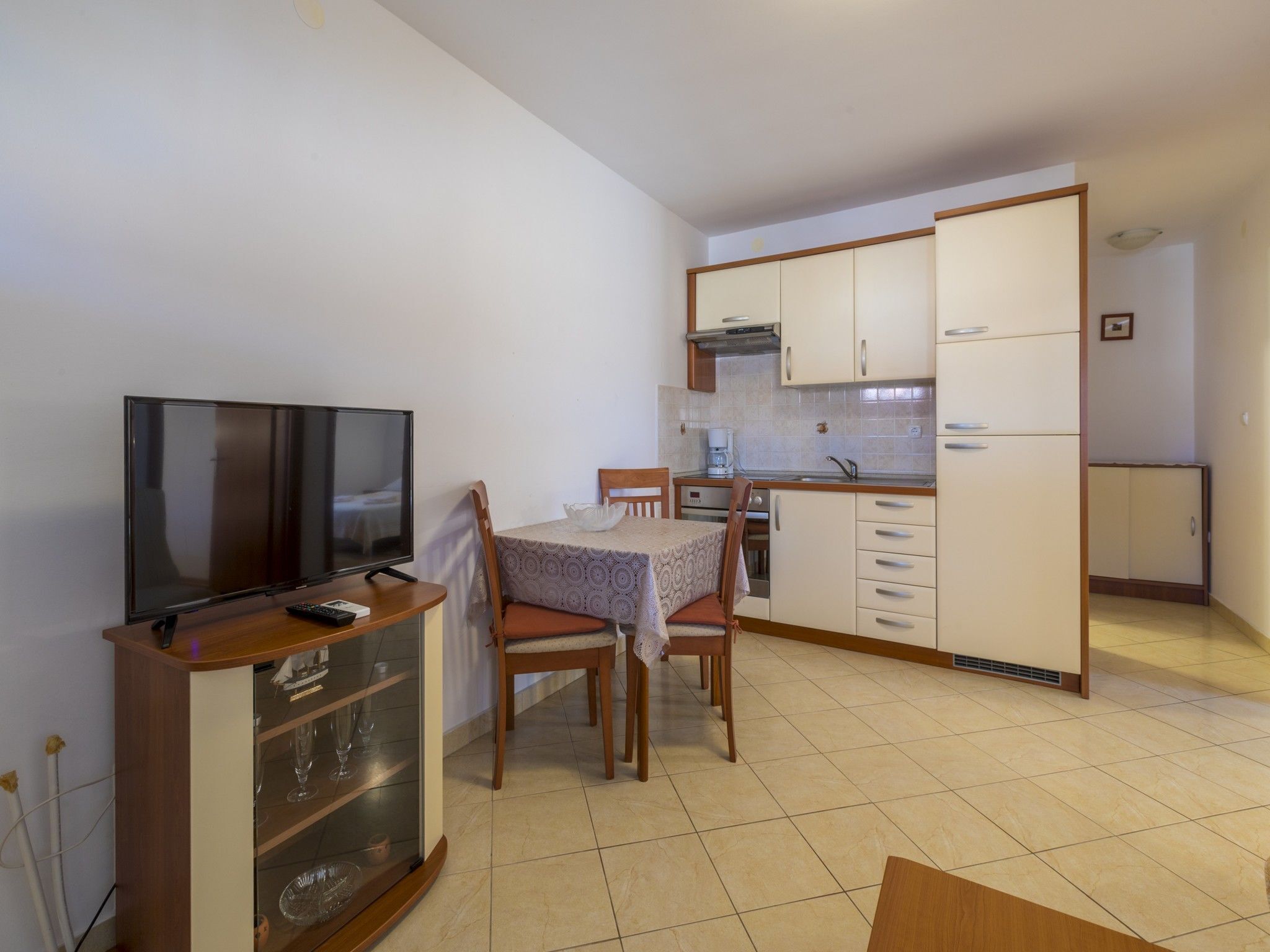 A compact kitchen with a dining area, a television, and a cabinet with glassware.