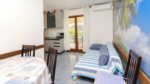 A room with a bed, a small table, and a kitchenette. There is a view of palm trees through the window. - Apartment Milena (Vodice)