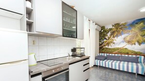 A modern kitchen with white cabinets, a built-in oven, and a dining area with a striped sofa. - Apartment Milena (Vodice)