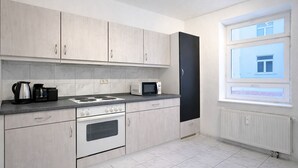 Eine moderne Küche mit hellen Holzschränken, einem schwarzen Kühlschrank, einem Herd, einer Mikrowelle und einem Wasserkocher.