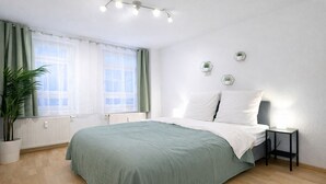 Ein Schlafzimmer mit Bett, Nachttisch, Topfpflanze und einem Fenster mit Vorhängen.
