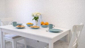 Ein weißer Esstisch mit einer Vase voller weißer Blumen, Schalen mit Speisen und einer Schale Orangen.