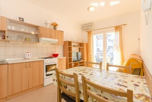 A compact kitchen with wooden cabinets, a stove, and a dining table with chairs. - Apartment Zdravko (Vodice)