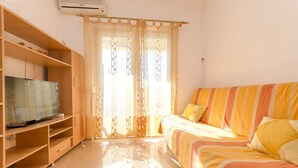 A room with a bed, a TV on a wooden stand, and a window with sheer curtains. - Apartment Zdravko (Vodice)