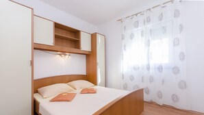 A bedroom with a bed, a wardrobe, a shelf, and a window with patterned curtains. - Apartment Zdravko (Vodice)