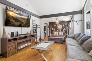 Ein Wohnzimmer mit Kamin, großem Fernseher, einer Couch und einer Kandelaber.