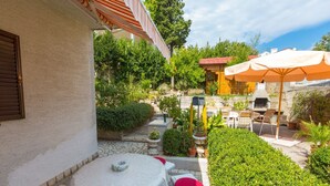 A patio with a round table and chairs, surrounded by greenery and a stone wall. - Apartment Darinka 1 (Crikvenica)