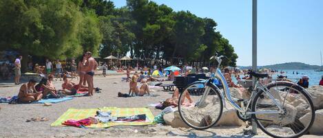 A beach with people sunbathing, a bicycle, and umbrellas.