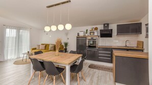A modern kitchen with a dining area, featuring a wooden table, black chairs, and a hanging light fixture. - Apartment Tarle (Vodice)