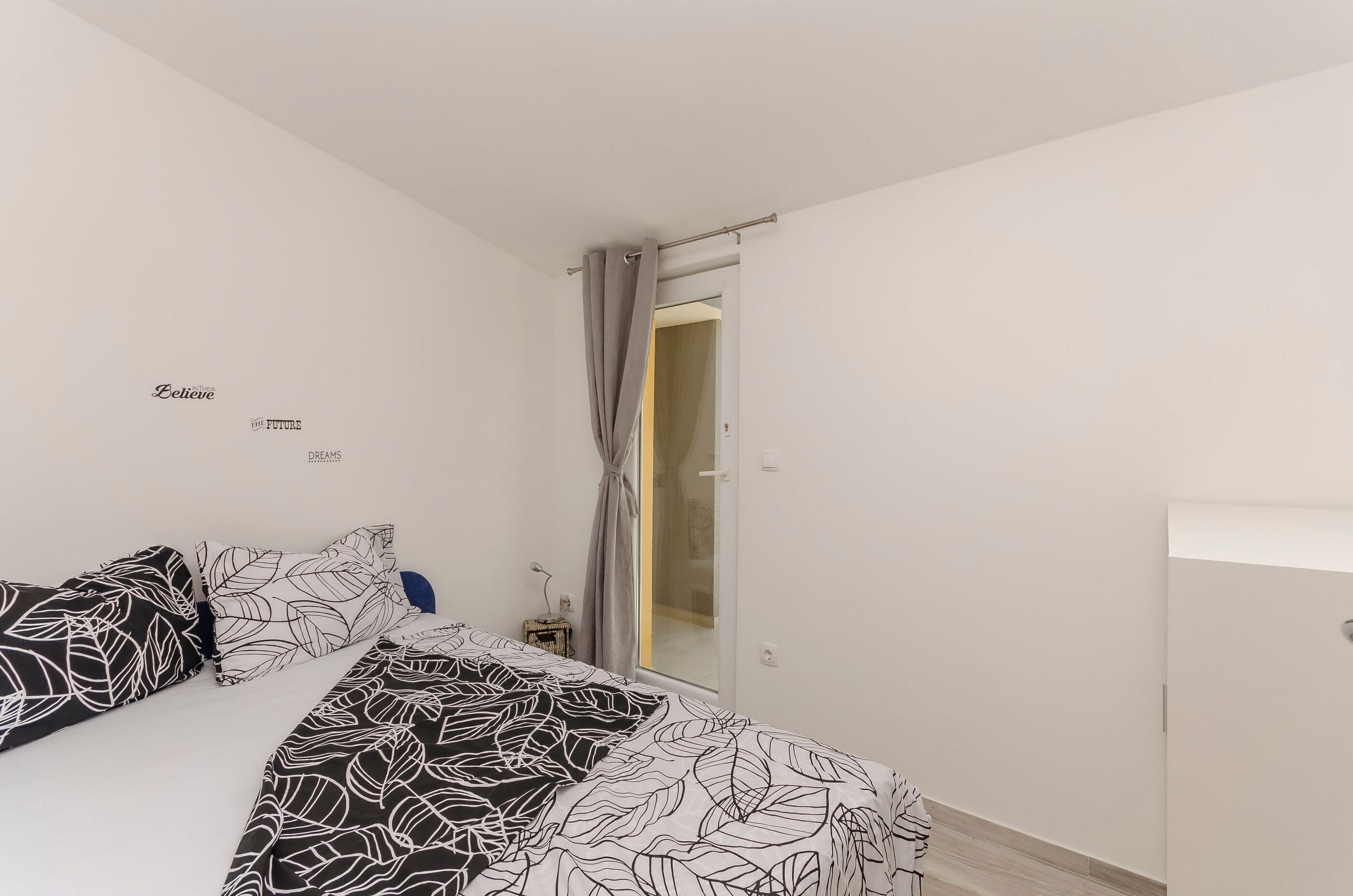 A bedroom with a bed, a nightstand, a wall with text, and a door leading to another room.