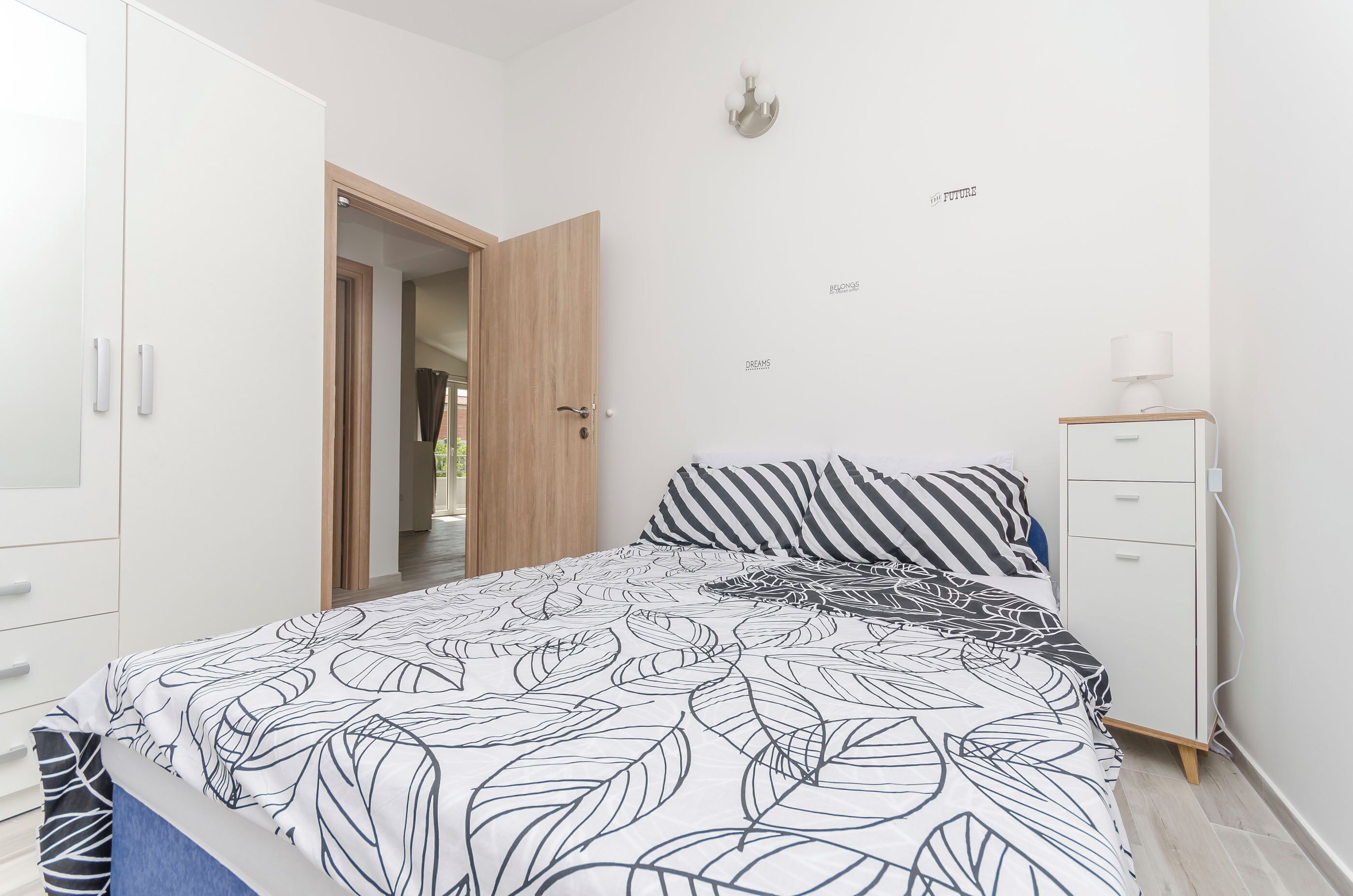 Un dormitorio con cama, armario, mesita de noche y lámpara de pared.