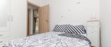 A bedroom with a bed, a wardrobe, a bedside table, and a wall-mounted light fixture.