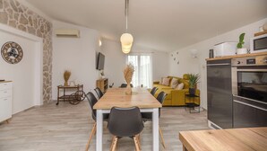 A modern kitchen with a built-in oven and microwave, a dining area with a wooden table and chairs, and a living room with a sofa and a TV. - Apartment Tarle (Vodice)