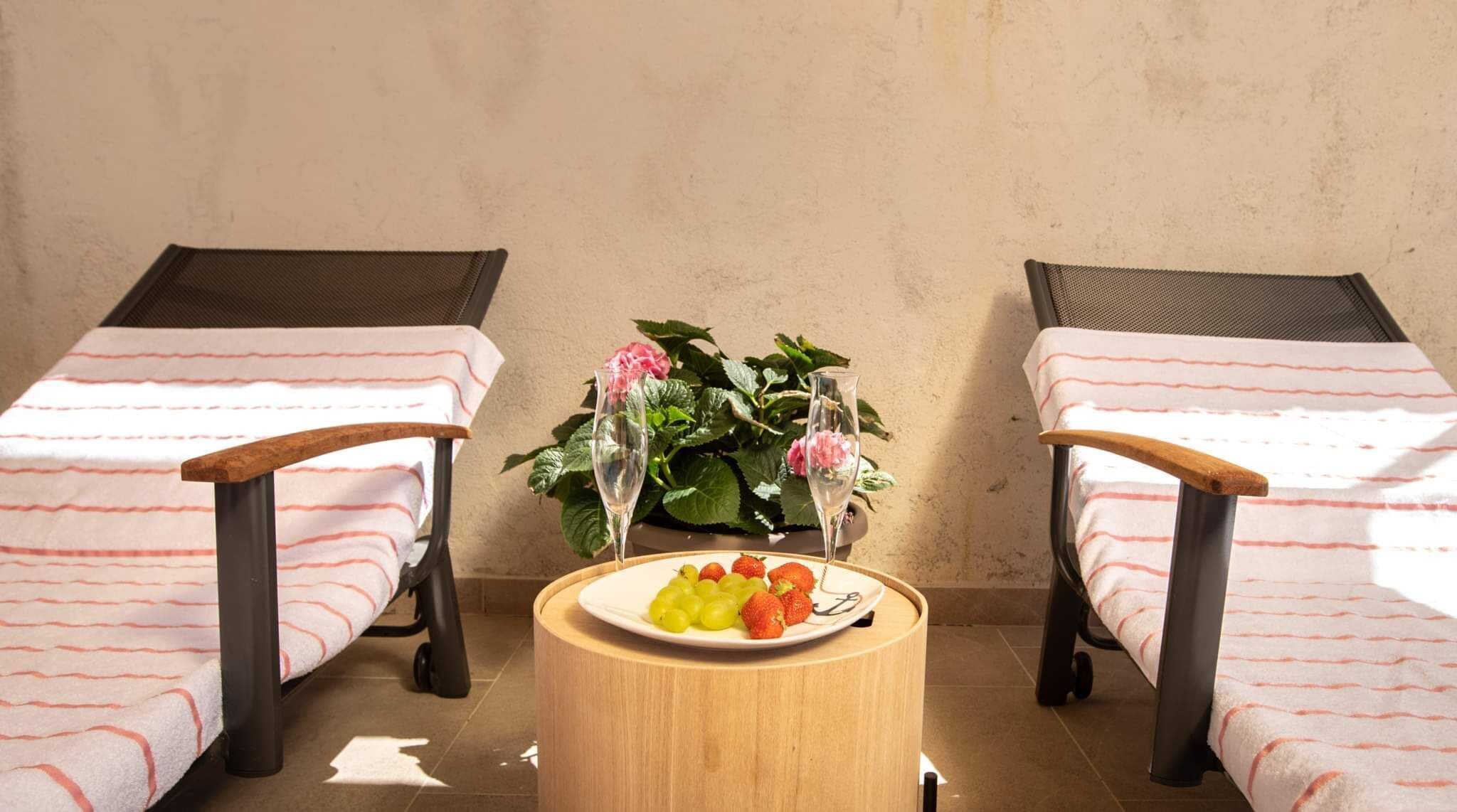 Ein Zimmer mit zwei Einzelbetten, einem kleinen runden Tisch mit einer Fruchtschale und einem Blumentopf mit Blumen.