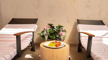 Ein Zimmer mit zwei Einzelbetten, einem kleinen runden Tisch mit einer Fruchtschale und einem Blumentopf mit Blumen.