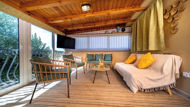 A cozy room with a wooden ceiling, a sofa with yellow pillows, a wicker chair, and a small table with a decorative item. - House Olive Tree (Rab)