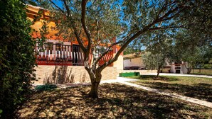 A courtyard with a tree, a brick pathway, and a building with orange walls. - House Olive Tree (Rab)