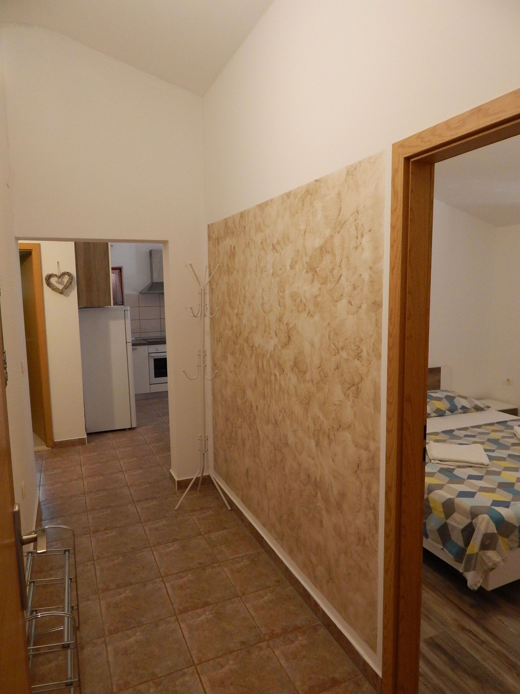 A room with a bed, a wooden door, and a kitchen area in the background.