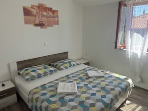 A bedroom with a bed, pillows, a nightstand, a window with curtains, and a wall-mounted picture. - Apartment Matilda (Starigrad)