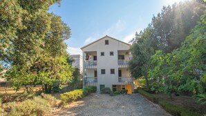 A two-story building with a central entrance, surrounded by greenery and a gravel path. - Apartments Barbara (Pakostane)