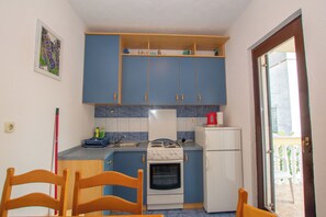 Μια μικρή κουζίνα με μπλε ντουλάπια, μια κουζίνα, ένα ψυγείο και μια τραπεζαρία με ξύλινες καρέκλες.