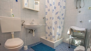 A bathroom with a toilet, sink, shower, and a blue mat on the floor. - Apartments Barbara (Pakostane)
