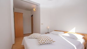 A bedroom with a wooden floor, a bed with white bedding and polka dot pillows, a nightstand with a lamp, and a wooden door. - Apartments Barbara (Pakostane)