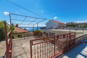 A rooftop terrace with a view of the sea, a red metal fence, and a white building with a red roof. - Apartment Kristina (Crikvenica)
