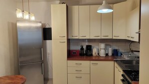 Eine kleine Küche mit Kühlschrank, Herd und Spüle. Es gibt Schränke, eine Arbeitsplatte und eine Pendelleuchte.