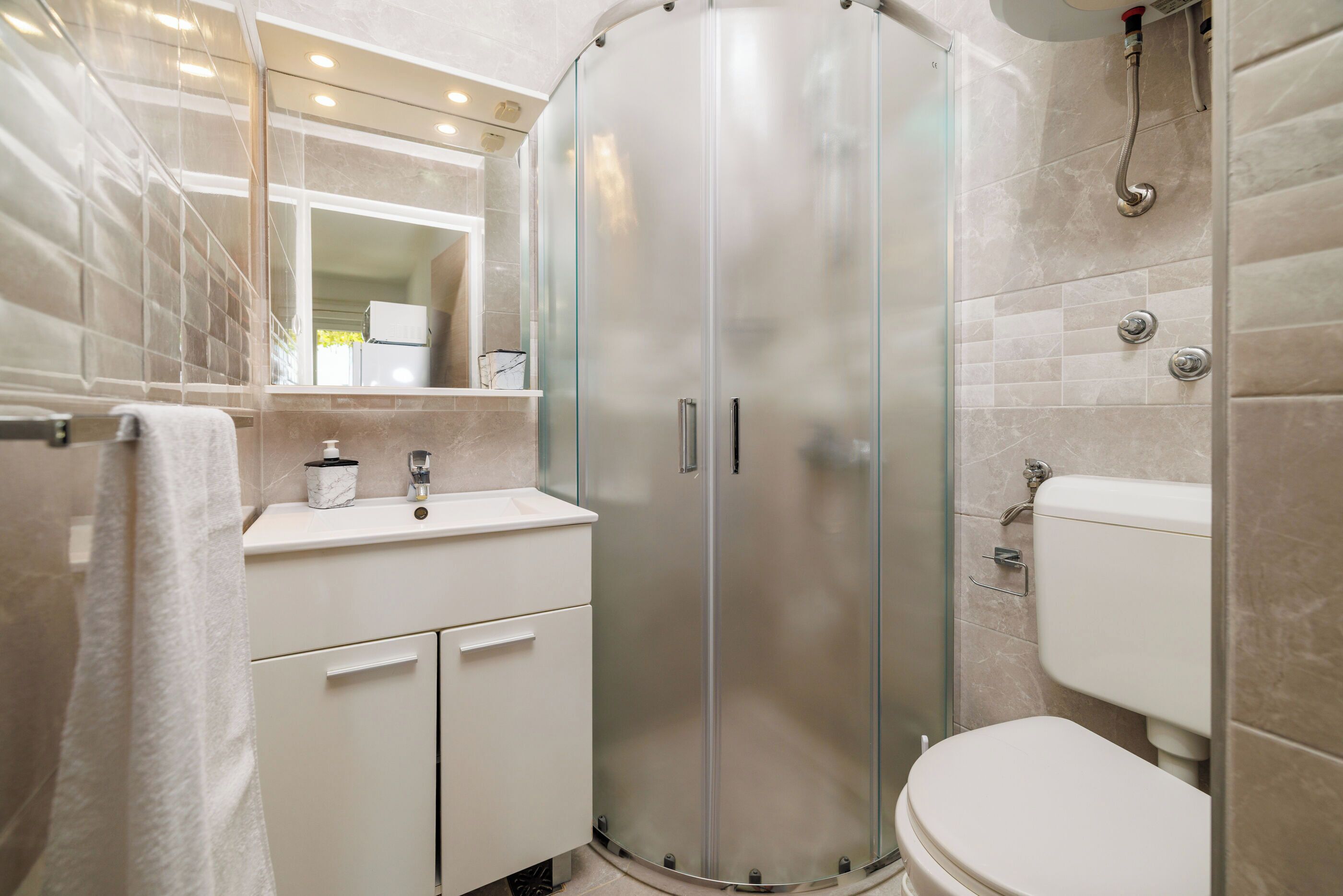 A modern bathroom with a glass-enclosed shower, a white sink with a marble countertop, and a toilet.