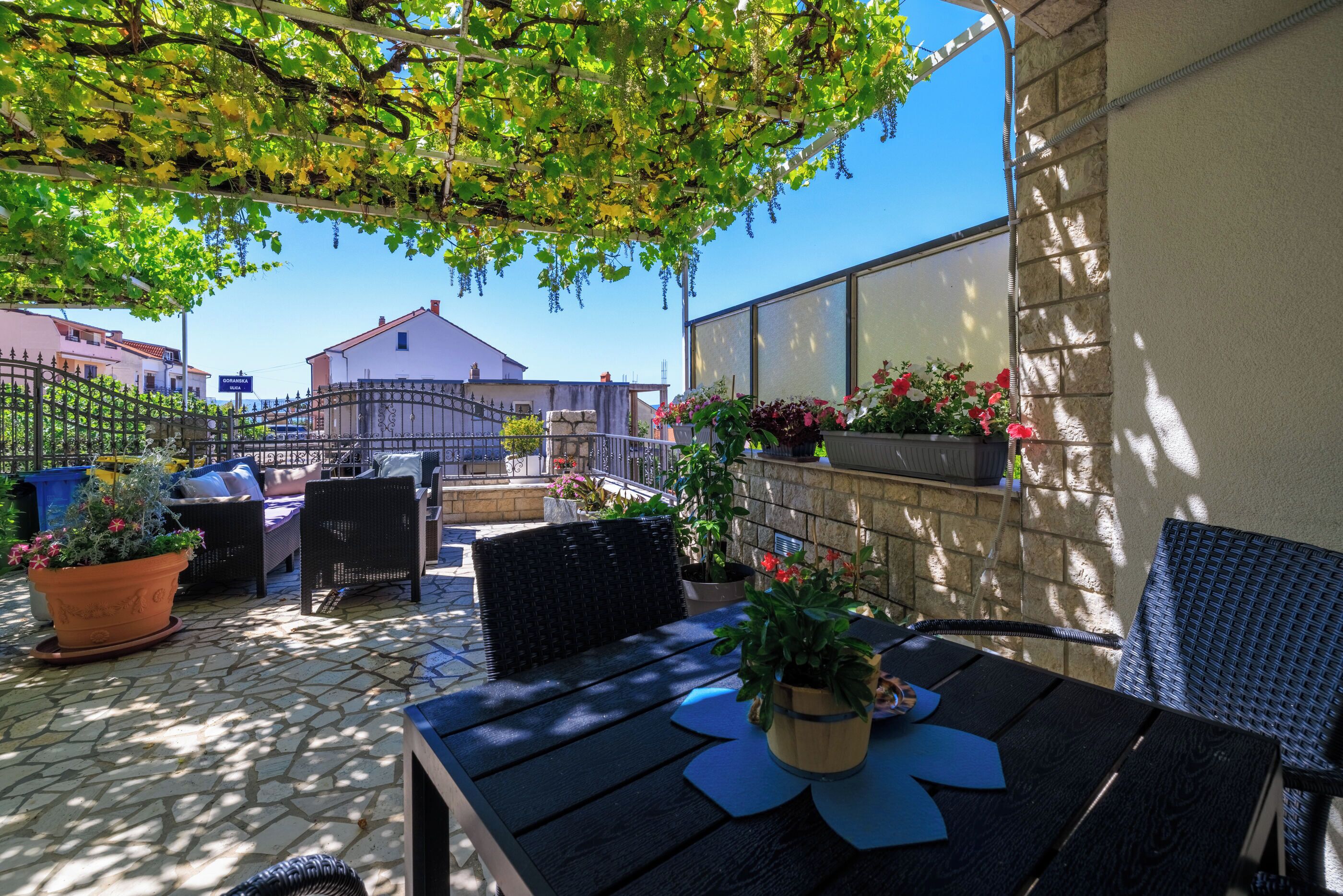 An outdoor patio with a table, chairs, potted plants, and a stone floor.