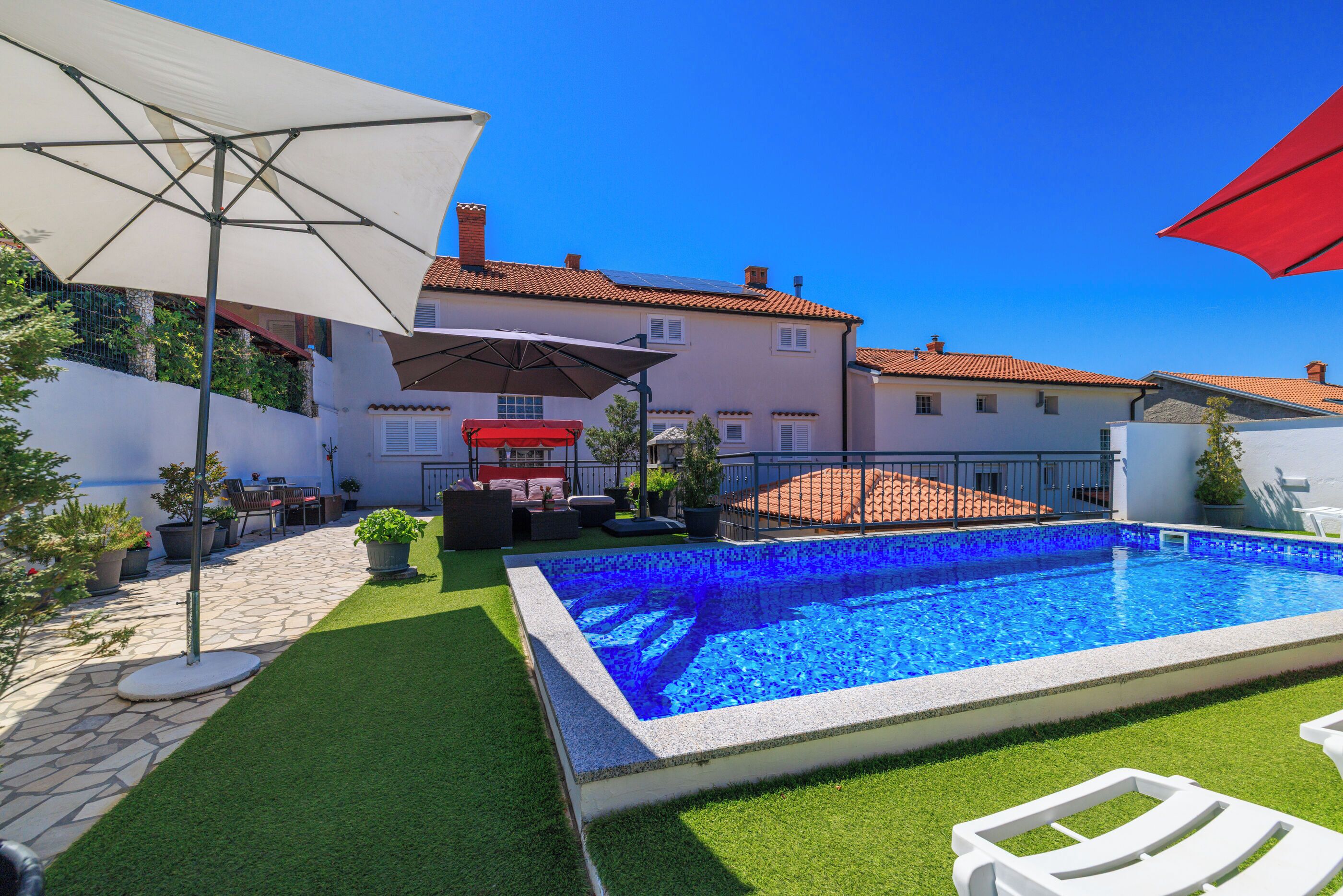 A swimming pool surrounded by a patio area with outdoor furniture and umbrellas.