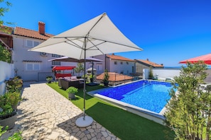 A swimming pool with a tiled deck, a covered seating area, and a view of the sea. - Apartments Grozdana (Crikvenica)