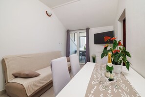 A modern living room with a sofa, a dining table with a floral table runner, a potted plant, and a bottle of champagne. - Apartments Grozdana (Crikvenica)