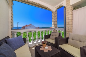 A balcony with wicker furniture, a white balustrade, and a view of a building and greenery. - Apartments Grozdana (Crikvenica)