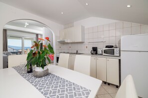 A modern kitchen with white cabinets, a dining table with a geometric table runner, a microwave, and a coffee maker. - Apartments Grozdana (Crikvenica)
