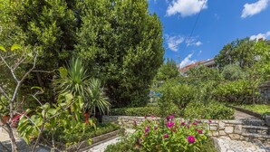A garden with stone pathways, various plants, and a stone wall. - Apartment Zeljka (Crikvenica)