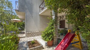 A courtyard with a red slide, potted plants, and a stone pathway. - Apartment Zeljka (Crikvenica)