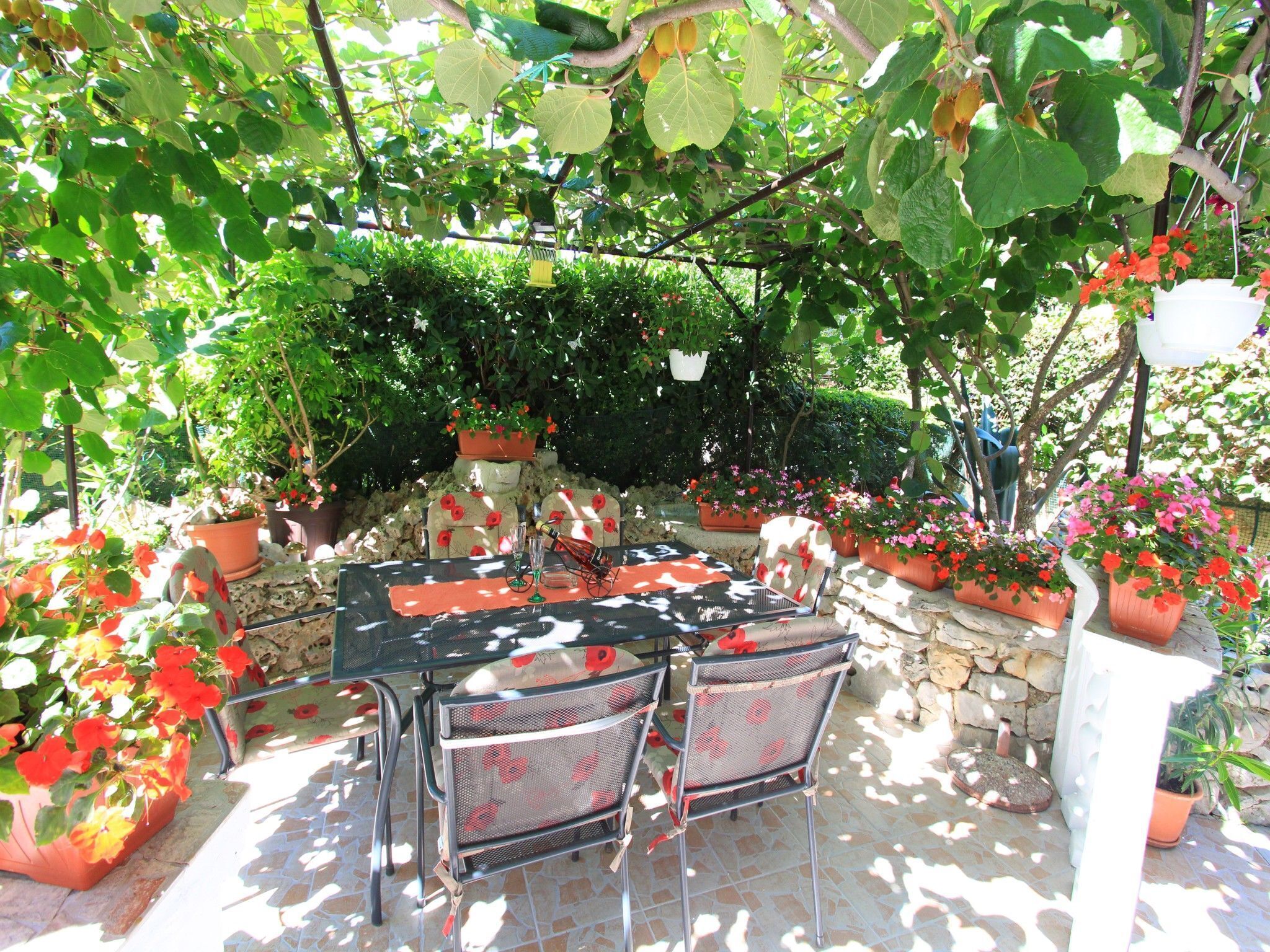 Un patio al aire libre con una mesa y sillas, rodeado de plantas en macetas y un muro de piedra.